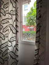Ventana entre cortinas de hojas con vistas a un árbol, setos y un edificio rojo del jardín
